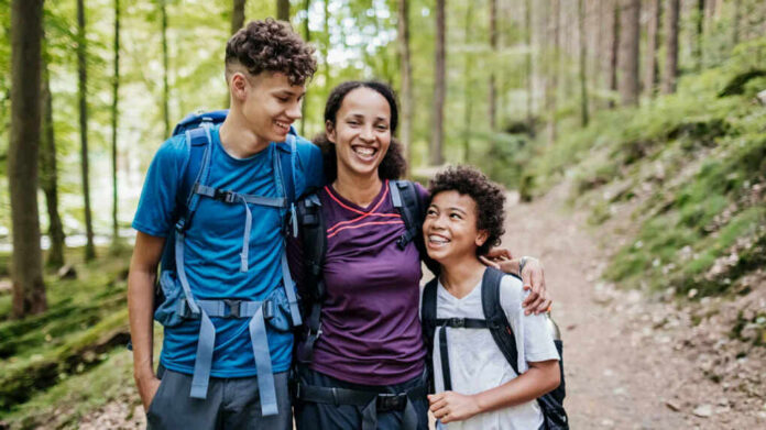 9a3727d6-ff70-4c52-bc15-2dd3fe515569_Test3495u10984501346 A mother and her two children smiling while hiking on a forest trail