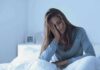 Woman sitting in bed with hand on face, looking tired