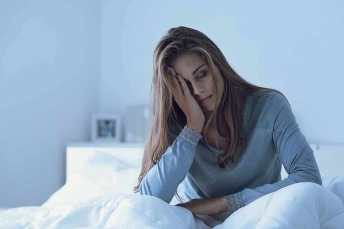 Woman sitting in bed with hand on face, looking tired
