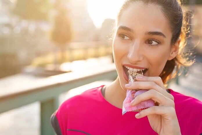 shutterstock_1367126105 Woman eating a granola bar outdoors