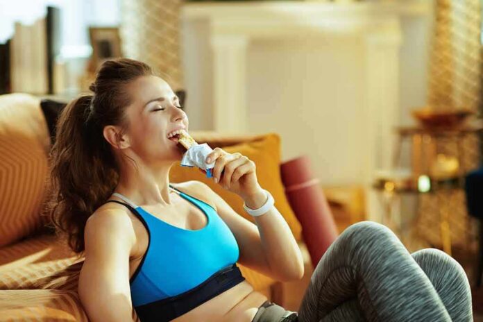 Woman in sportswear eating a snack bar on a couch