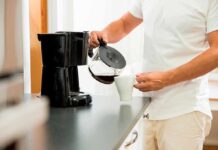 Person pouring coffee from carafe into mug beside drip coffee maker