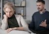 Woman on couch looking away as man gestures during argument