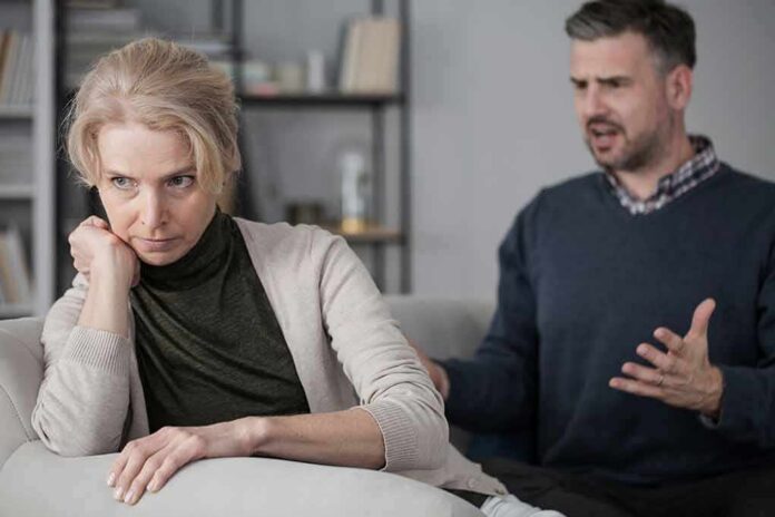 Woman on couch looking away as man gestures during argument