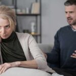 Upset woman sitting on couch while man gestures behind her