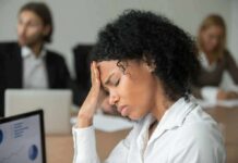 Constant Fatigue? Check These Hormones First Woman in office holding her head with eyes closed