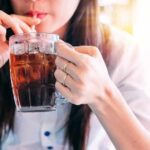 person sipping iced drink from a glass mug with a straw