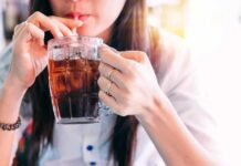 person sipping iced drink from a glass mug with a straw