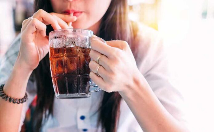 person sipping iced drink from a glass mug with a straw