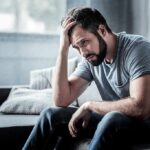 Man sitting on couch with head in hand
