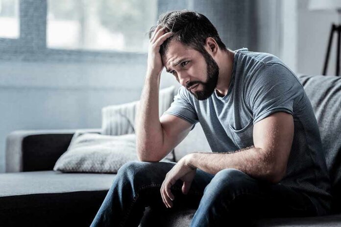 shutterstock_1060449161 Man sitting on couch with head in hand