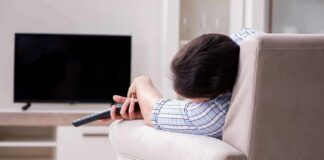 Person lying on a sofa holding a TV remote