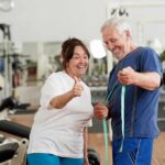 Older man and woman smiling with measuring tape in a gym