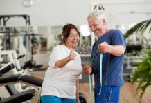 Older man and woman smiling with measuring tape in a gym