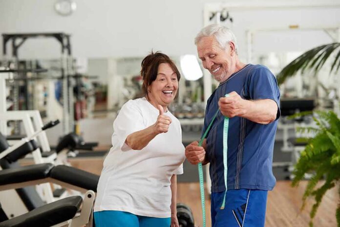 shutterstock_1395947015 Older man and woman smiling with measuring tape in a gym