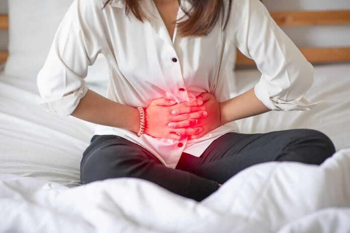 shutterstock_1456631798 Woman holding her abdomen in pain while sitting on a bed