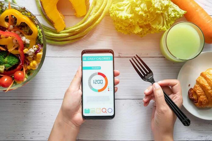 shutterstock_1465238459-2 hands holding phone with calorie tracker beside salad and pastry