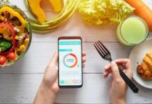 hands holding phone with calorie tracker beside salad and pastry