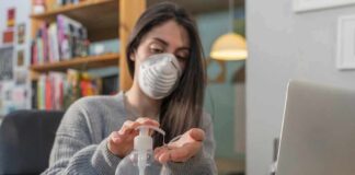 Woman wearing a mask uses hand sanitizer at a desk with a laptop