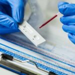 Gloved hands using a rapid test cassette with a blood sample dropper