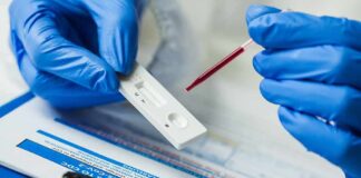 Gloved hands using a rapid test cassette with a blood sample dropper