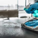Gloved hands spraying and wiping a tabletop