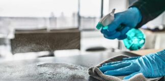 Gloved hands spraying and wiping a tabletop