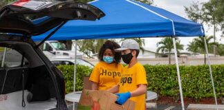 Volunteers load a box into a car under a blue canopy