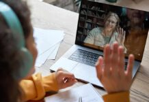 Student in headphones waving at a person on a laptop video call