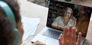 Student in headphones waving at a person on a laptop video call