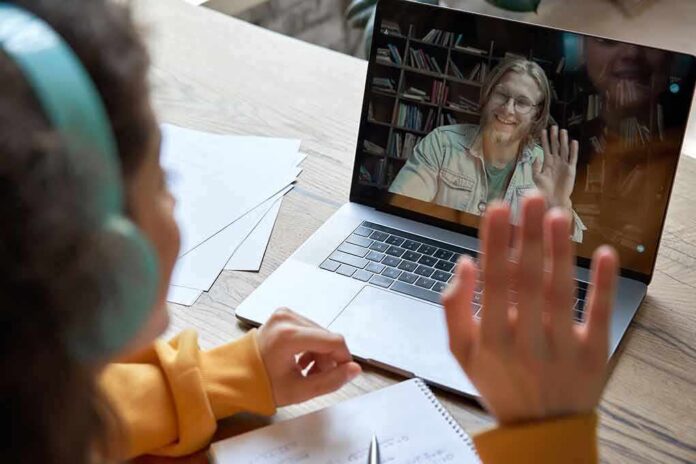 shutterstock_1738498550 Student in headphones waving at a person on a laptop video call