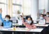 Measles Outbreak Wave Hits Classrooms Schoolchildren wearing masks raise hands in a classroom