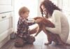 toddler petting orange cat held by woman on kitchen floor
