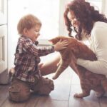 toddler petting orange cat held by woman on kitchen floor