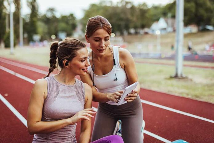 shutterstock_2554610065 Two women at a running track looking at a tablet