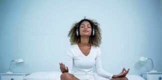 Woman meditating cross-legged on bed wearing headphones