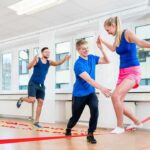 woman balancing on a slackline indoors with two men assisting