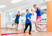 woman balancing on a slackline indoors with two men assisting