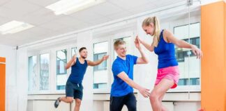 woman balancing on a slackline indoors with two men assisting