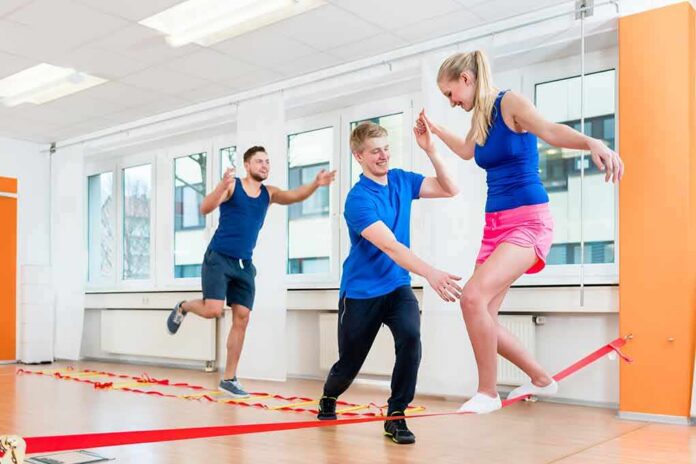 shutterstock_567688111 woman balancing on a slackline indoors with two men assisting