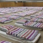 rows of mattresses with striped bedding in a large hall