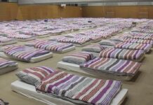 rows of mattresses with striped bedding in a large hall