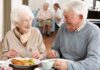 Two seniors smiling while eating a meal together at a table