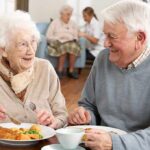 Two seniors smiling while eating a meal together at a table