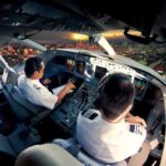 Pilots in an airplane cockpit during city approach at sunset
