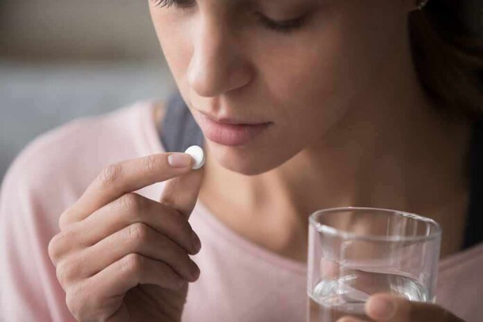 1783889694099-0lovxz-shutterstock-1477334069-1 Woman holding a white pill and a glass of water