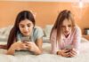 Social Media: Pediatricians Ditch Time Limits Two girls lying on a bed using smartphones