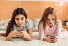 Social Media: Pediatricians Ditch Time Limits Two girls lying on a bed using smartphones