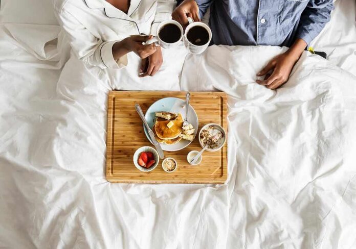 shutterstock_1029691264 Breakfast in bed with two people holding coffee