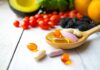 Common Vitamin Delivers Surprising Cancer Punch Wooden spoon holding assorted vitamin pills beside fresh fruits and vegetables